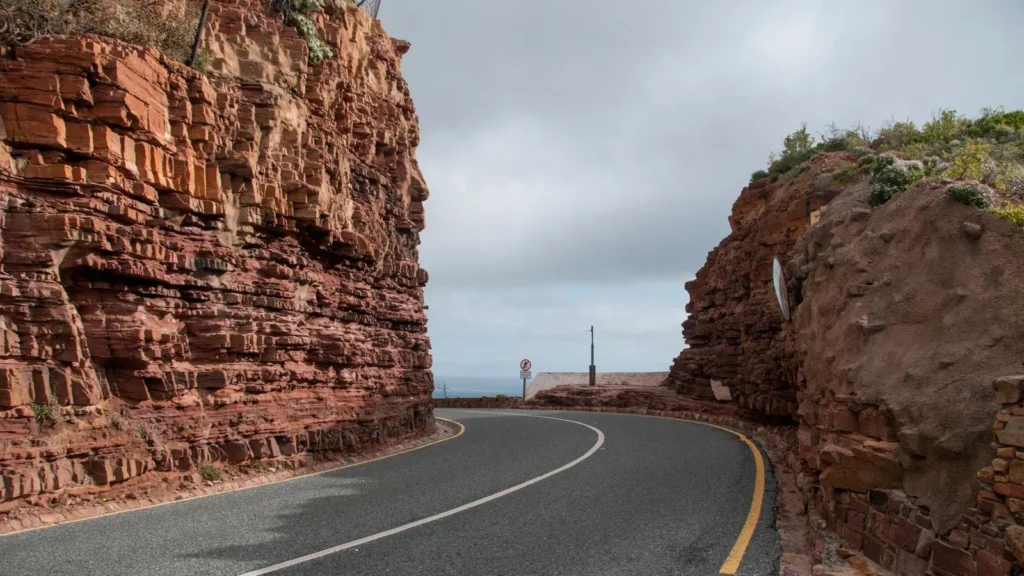 Cape Town'da Chapman’s Peak yakınında kırmızı kayalıklar arasından kıvrılan yol
